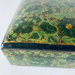 K&ouml;nnte beinhalten: Eine gr&uuml;n und gold bemalte Holzkiste mit floralem Design. Die Kiste hat einen Scharnierdeckel und ist mit filigranen Details verziert.