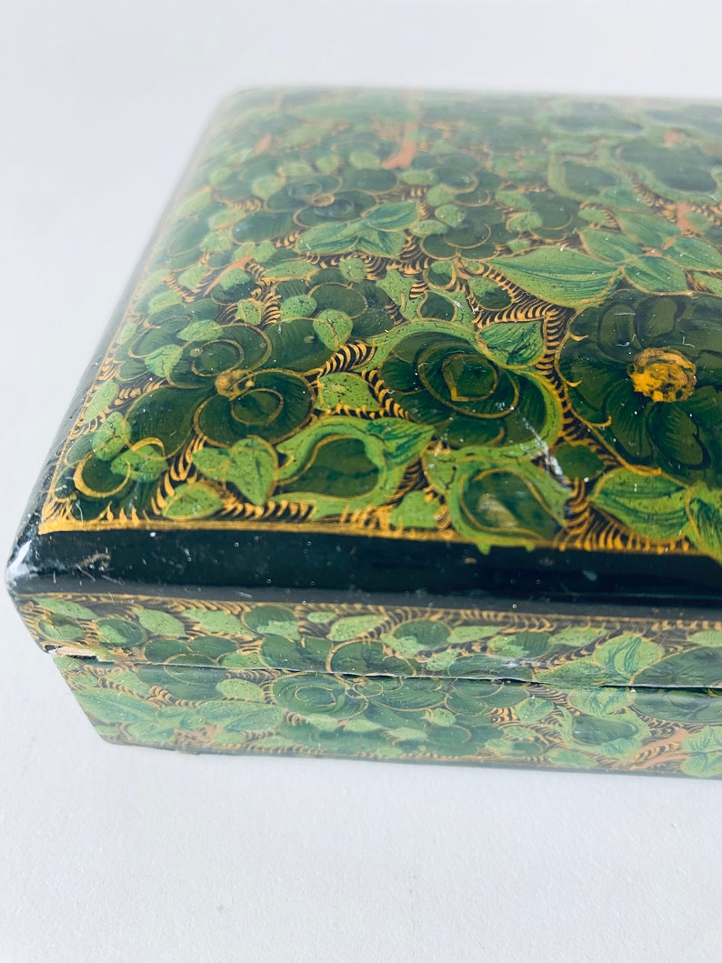 K&ouml;nnte beinhalten: Eine gr&uuml;n und gold bemalte Holzkiste mit floralem Design. Die Kiste hat einen Scharnierdeckel und ist mit filigranen Details verziert.