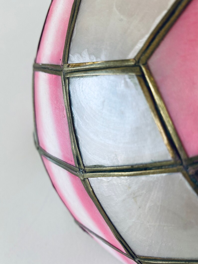 Puede incluir: Una pantalla de l&aacute;mpara geom&eacute;trica rosa y blanca con un marco de lat&oacute;n. La pantalla est&aacute; hecha de un material transl&uacute;cido y tiene un aspecto delicado y femenino.