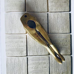 May include: A gold-coloured nutcracker with a long handle, lying on a white surface with a pattern of fish. The surface is made up of square tiles.