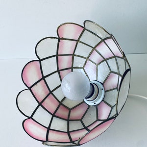 Puede incluir: Una pantalla de l&aacute;mpara rosa y blanca con un patr&oacute;n geom&eacute;trico. La pantalla est&aacute; hecha de un material delgado y transl&uacute;cido y tiene un borde festoneado.