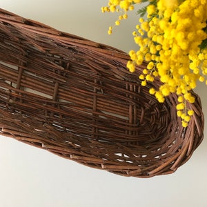 Puede incluir: Una cesta de mimbre marr&oacute;n con un dise&ntilde;o tejido. La cesta tiene forma ovalada y un acabado liso y natural.