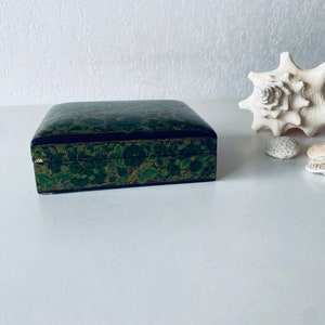 May include: A small, rectangular box with a black base and a green and gold floral design. The box is made of wood and has a hinged lid.