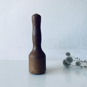 May include: A wooden muddler, a kitchen tool for mixing drinks, with a rounded handle and a cylindrical base. The muddler is made of dark brown wood and has a smooth, polished finish. It is designed for mixing ingredients in cocktails or other beverages.