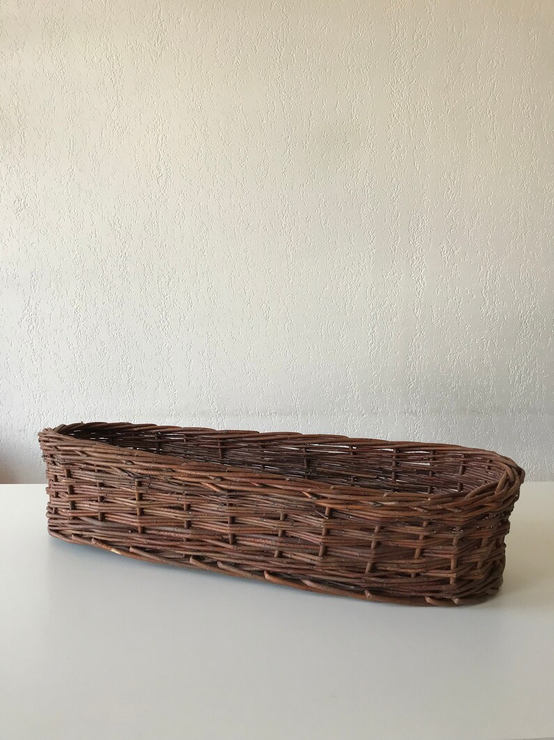 Puede incluir: Una cesta de mimbre larga y marr&oacute;n con un dise&ntilde;o tejido. La cesta tiene forma ovalada y un acabado liso y natural.