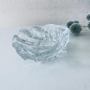Peut inclure: Un cendrier en verre transparent avec un design ondulé et texturé. Le cendrier a la forme d'une coquille.