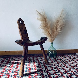 May include: A rustic wooden chair with a unique design and three legs. The chair is sitting on a colourful patterned rug.