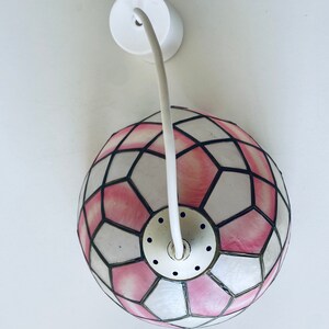 Puede incluir: Una l&aacute;mpara colgante de cristal de colores rosa y blanco con un cable blanco y una montura de techo.