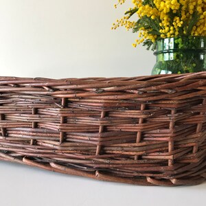 Puede incluir: Una cesta de mimbre marr&oacute;n con un patr&oacute;n tejido. La cesta est&aacute; vac&iacute;a y se encuentra sobre una superficie blanca.