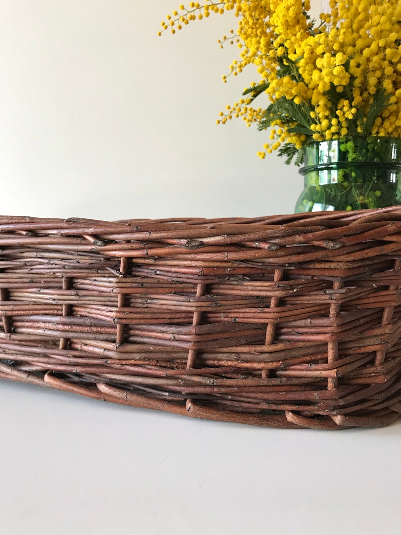 Puede incluir: Una cesta de mimbre marr&oacute;n con un patr&oacute;n tejido. La cesta est&aacute; vac&iacute;a y se encuentra sobre una superficie blanca.