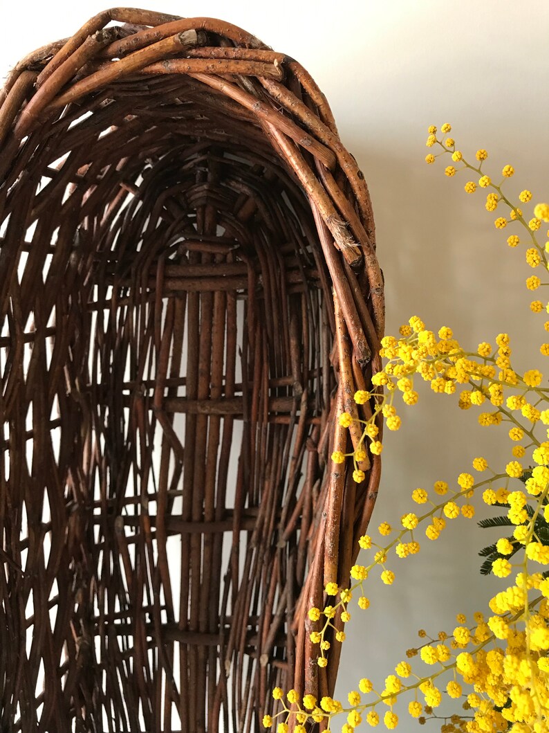 Puede incluir: Una cesta de mimbre tejida con forma ovalada redondeada. La cesta est&aacute; hecha de ramitas marrones naturales y tiene un patr&oacute;n tejido.