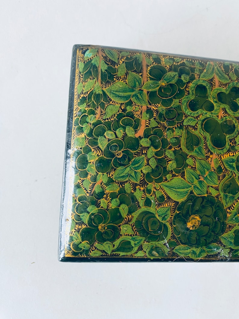 K&ouml;nnte beinhalten: Eine gr&uuml;n und gold bemalte Holzkiste mit einem floralen Design. Die Kiste ist mit komplizierten Details verziert und hat einen traditionellen indischen Stil.