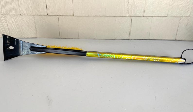 May include: A black and yellow ice scraper with a long, patterned handle. The scraper has a black blade with a hole and a yellow brush. The handle is yellow with a green and blue design.