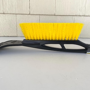 May include: A black and yellow snow brush with a yellow brush head and a black scraper blade. The brush has a long handle for reaching across a car windscreen. The brush is designed for removing snow and ice.