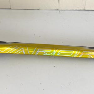 May include: A close-up of a yellow hockey stick with the word "VAPOR" printed in white. The stick has a black accent on the top edge. The background is a plain white surface.