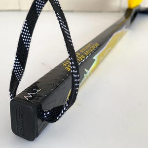 May include: Black and yellow hockey stick with the text "Reactive R Lancer" and a black and white patterned loop. The stick has the brand name "Bauer" on the end.