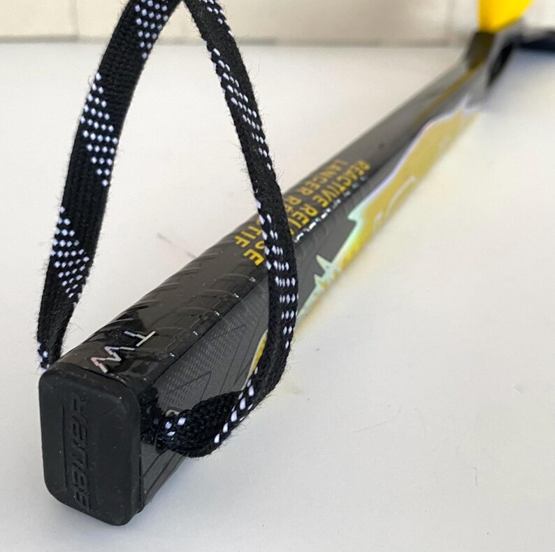May include: Black and yellow hockey stick with the text "Reactive R Lancer" and a black and white patterned loop. The stick has the brand name "Bauer" on the end.