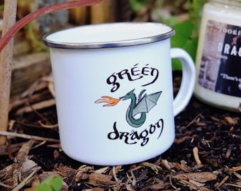 Può includere: Una tazza di smalto bianco con un design di drago verde e il testo "green dragon" in un font stilizzato. Il drago sta respirando fuoco.