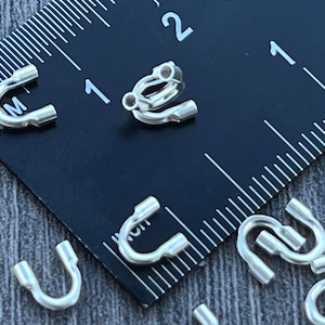 Op de afbeelding: Close-up van zilverkleurige metalen springringen, met een diameter van 2,5 cm, tegen een zwarte liniaal. De springringen worden gebruikt voor het maken van sieraden.