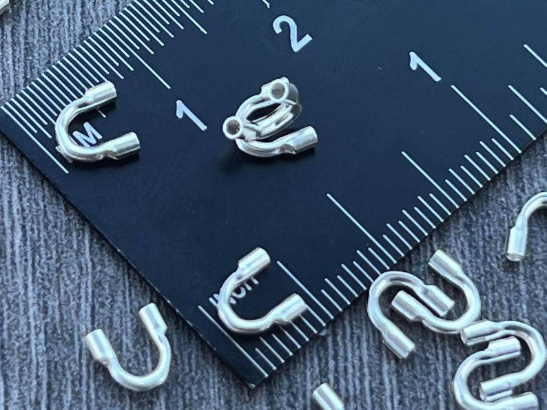 Op de afbeelding: Close-up van zilverkleurige metalen springringen, met een diameter van 2,5 cm, tegen een zwarte liniaal. De springringen worden gebruikt voor het maken van sieraden.