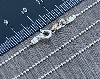 May include: A silver ball chain necklace with a lobster clasp closure. The chain is laid out on a ruler, showing the length of the necklace.
