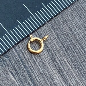 Pode incluir: Fecho de metal dourado com um anel redondo e um fecho de mola. O fecho &eacute; projetado para prender joias ou outros itens.