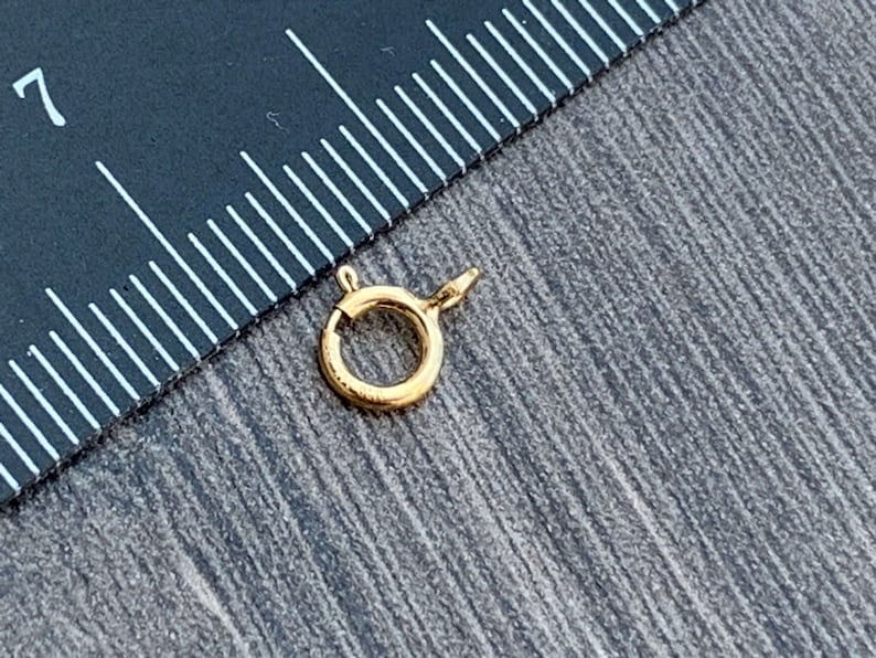 Pode incluir: Fecho de metal dourado com um anel redondo e um fecho de mola. O fecho &eacute; projetado para prender joias ou outros itens.