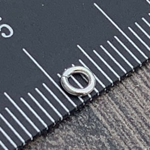 May include: A silver jump ring measuring approximately 5/16 inch in diameter. The jump ring is shown next to a ruler with markings in inches.