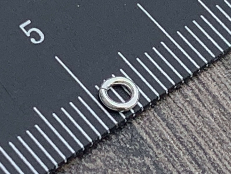 May include: A silver jump ring measuring approximately 5/16 inch in diameter. The jump ring is shown next to a ruler with markings in inches.