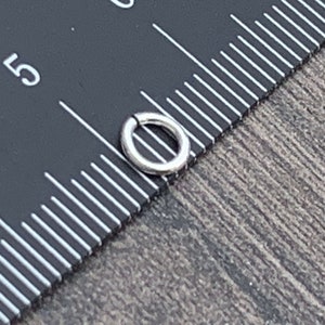 May include: A silver jump ring measuring 5/16 inch in diameter, shown next to a ruler.