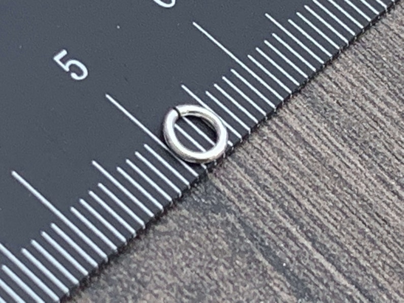 May include: A silver jump ring measuring 5/16 inch in diameter, shown next to a ruler.