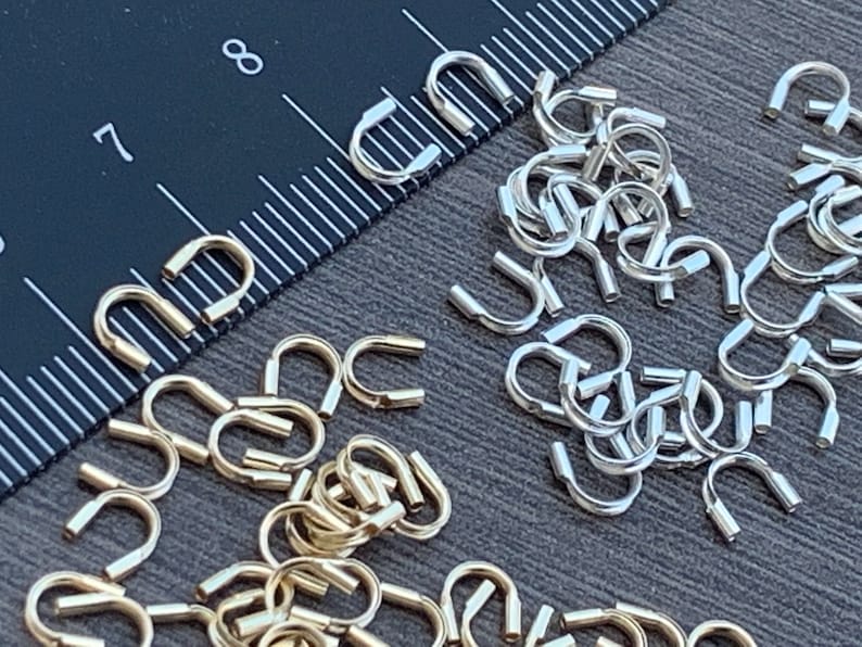 Op de afbeelding: Een close-up afbeelding van twee stapels kleine, metalen, U-vormige springringen. De ene stapel is goud en de andere is zilver.