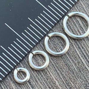 May include: Four silver jump rings of different sizes, measured against a ruler.