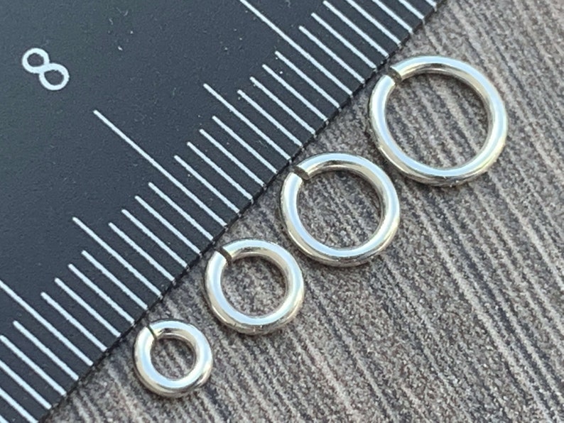 May include: Four silver jump rings of different sizes, measured against a ruler.