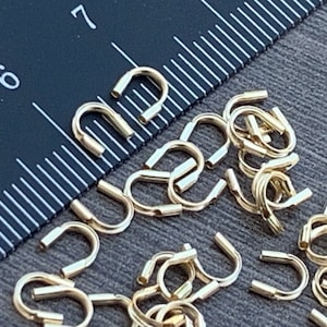 Op de afbeelding: Een close-up van een stapel gouden metalen springringen. De ringen hebben een diameter van ongeveer 1,2 cm en een gladde, gepolijste afwerking.