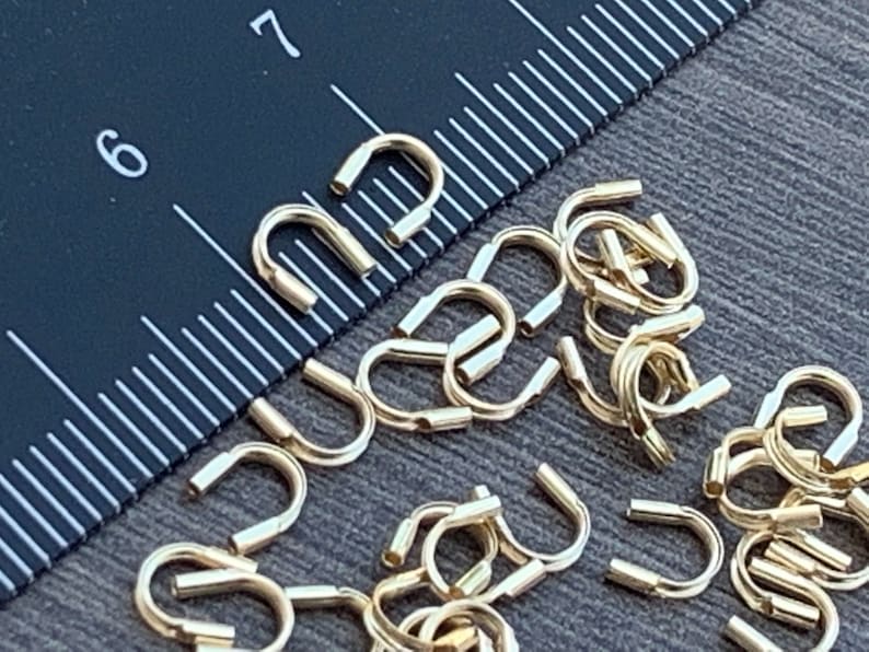 Op de afbeelding: Een close-up van een stapel gouden metalen springringen. De ringen hebben een diameter van ongeveer 1,2 cm en een gladde, gepolijste afwerking.