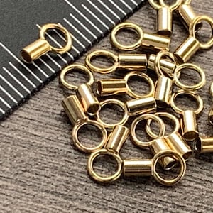 May include: A pile of gold-colored metal jump rings with a small cylinder attached to each ring. The rings are about 1/2 inch in diameter.