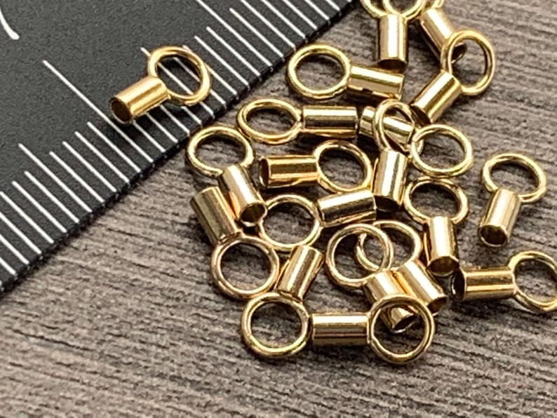 May include: A pile of gold-colored metal jump rings with a small cylinder attached to each ring. The rings are about 1/2 inch in diameter.