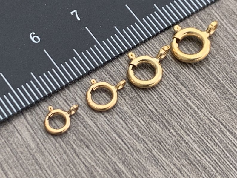 Pode incluir: Quatro fechos de lagosta de metal dourado de tamanhos diferentes. Os fechos est&atilde;o dispostos em uma fila do maior para o menor. Uma r&eacute;gua &eacute; vis&iacute;vel no fundo.