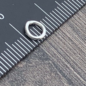 May include: A silver jump ring, approximately 5 mm in diameter, is shown next to a ruler.