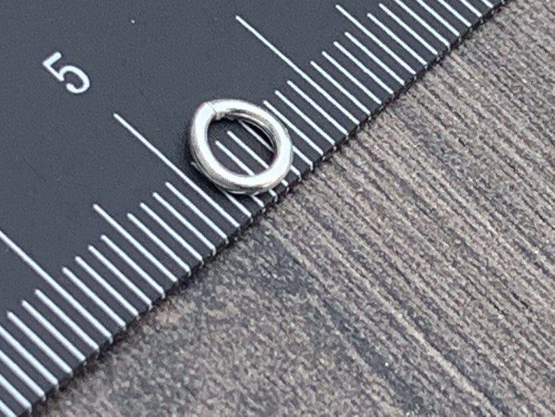 May include: A silver jump ring, approximately 5 mm in diameter, is shown next to a ruler.