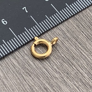 Pode incluir: Fecho de metal dourado com fecho de mola. O fecho tem um di&acirc;metro de aproximadamente 2,5 cm.
