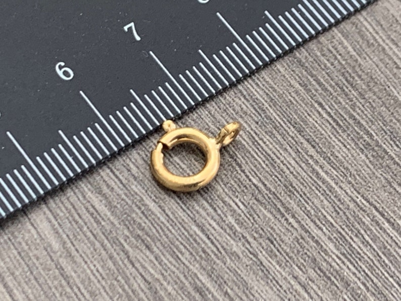 Pode incluir: Fecho de metal dourado com fecho de mola. O fecho tem um di&acirc;metro de aproximadamente 2,5 cm.