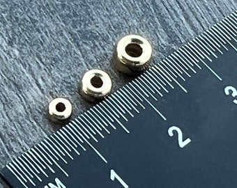 Può includere: Tre anelli di metallo dorati di diverse dimensioni, allineati su un righello nero con segni bianchi. Il righello mostra le misure in pollici.