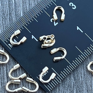 Op de afbeelding: Gouden metalen krimpkralen voor het maken van sieraden. De kralen worden getoond naast een liniaal, waarbij de grootste kraal ongeveer 1,2 cm in diameter is.