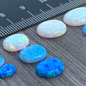May include: A collection of oval-shaped opals in various sizes. The opals range in color from white to blue.