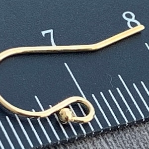 May include: A gold-toned earring hook with a small ball at the end. The hook is measured against a ruler, showing it is slightly over 7/8 of an inch long.