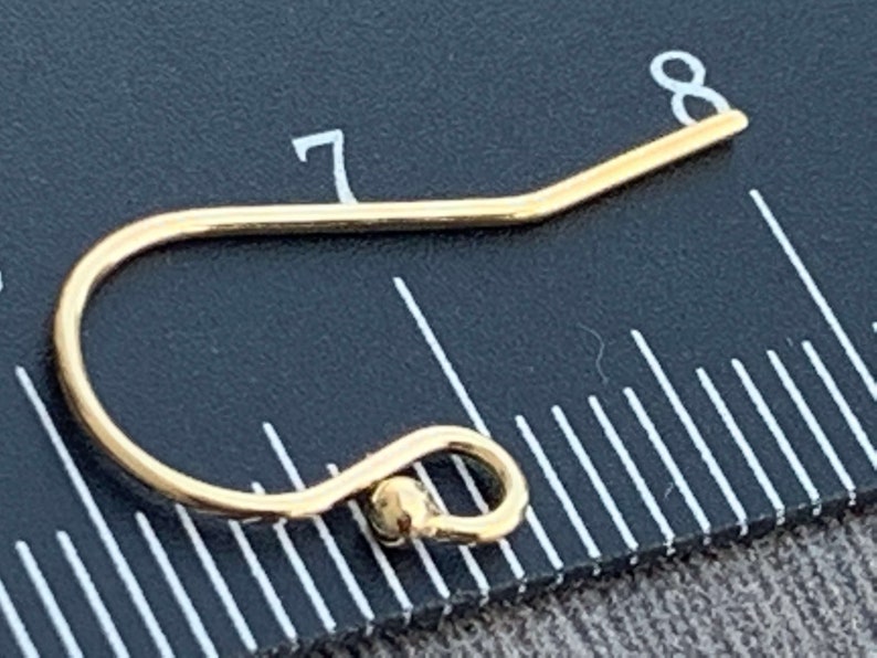 May include: A gold-toned earring hook with a small ball at the end. The hook is measured against a ruler, showing it is slightly over 7/8 of an inch long.
