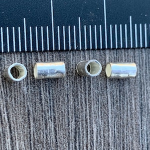 May include: Four silver-colored metal tube beads, two with a round hole and two with a hexagonal hole.