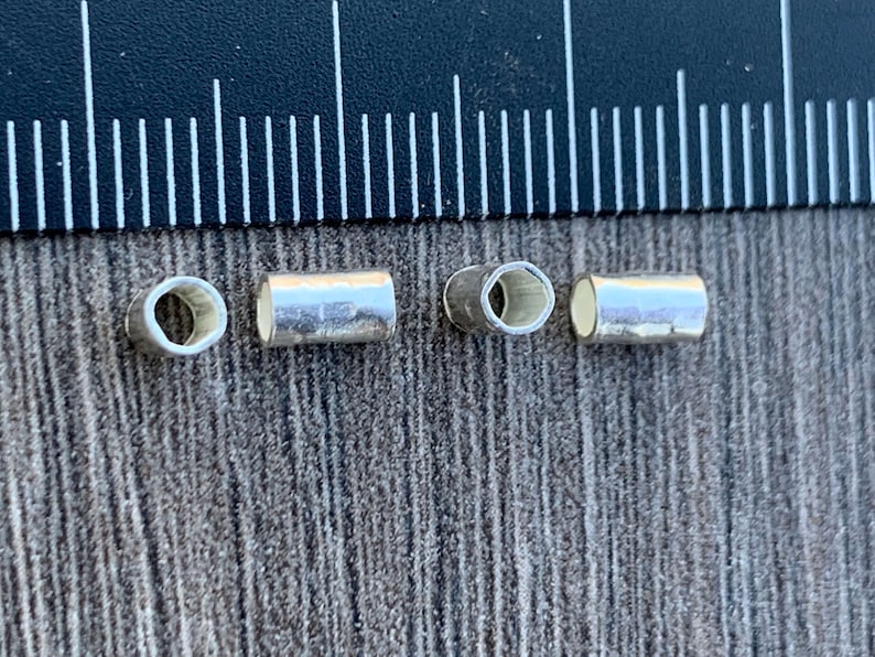 May include: Four silver-colored metal tube beads, two with a round hole and two with a hexagonal hole.